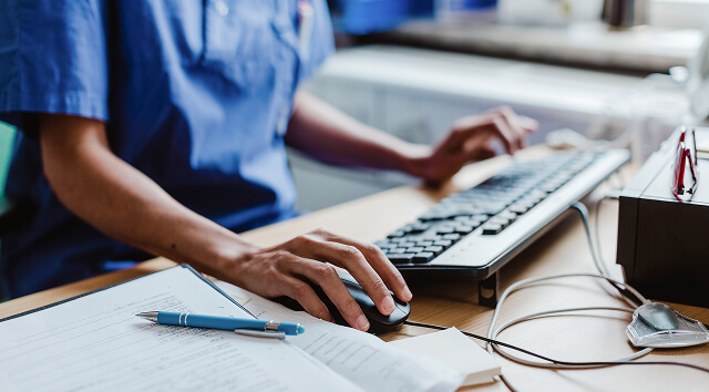 Close-up of a healthcare professional in scrubs typing on a computer.